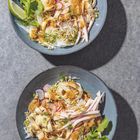 Zwei Schalen mit Nudelsalat, garniert mit Radieschen, Sprossen, Limettenscheiben und frischen Kräutern auf grauer Fläche.