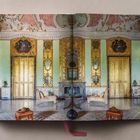 Offene Seite eines Buches zeigt einen opulenten Raum mit goldenen Türen, verzierten Wänden und eleganten Möbeln.