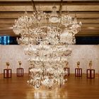 Kronleuchter dominiert den Raum. Vergoldete Tierköpfe auf Sockeln bilden einen Kreis um das Zentrum auf Holzboden.