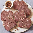 Auf einem runden Teller liegen mehrere Scheiben rotbraunes Nussbrot, daneben eine kleine Schale mit Pekannüssen.