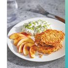 Seite 143. Ein Teller Kartoffelpuffer mit Gurkensalat und Pfirsichscheiben. Ein Glas Wasser und Gabel im Hintergrund.