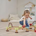 Ein kleines Mädchen spielt auf dem Boden mit einer Holzkugelbahn in einem minimalistischen Raum.