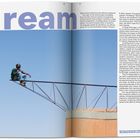 Text: "dream" in großen Buchstaben. Ein Mann sitzt auf einem Metallträger über einem Dach. Blauer Himmel im Hintergrund.