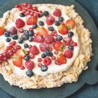 Kuchen mit Sahne, roten und blauen Beeren, auf einem dunklen Teller, umgeben von Mandelblättchen.