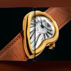 Verzerrte goldene Uhr mit römischen Ziffern, braunes Lederarmband, auf einer aufgeschlagenen Zeitschrift.