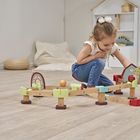 Ein Mädchen spielt auf dem Boden mit einer bunten Spielzeugbahn aus Holz in einem hellen Raum mit Holzfußboden.