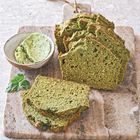 Grünes Brot auf Holzbrett, daneben eine Schale mit Kräuterbutter und eine Petersilienblätter.