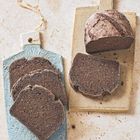 Keine sichtbaren Texte. Zwei Holzbrettchen mit dunkelbraunem Brot: eins mit geschnittenen Scheiben, das andere mit einem halben Laib.