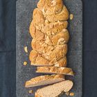 Ein geflochtener Hefezopf mit Mandelblättchen auf einem dunklen Untergrund, teilweise aufgeschnitten.