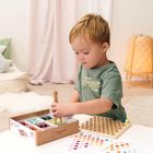 Ein Junge spielt mit bunten Holzperlen und einem Steckbrett. Im Hintergrund ist Dekoration mit Kissen und Lampe zu sehen.