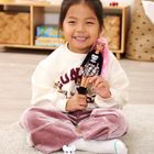 Ein Kind hält eine Puppe mit rosa Haaren. Im Hintergrund ein Regal mit Büchern und Körben. Auf dem Boden Spielzeug.