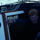 Zwei Instrumente zeigen Windgeschwindigkeit und Richtung. Eine Person mit durchnässtem Gesicht taucht aus einer Kajüte auf.