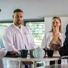 Mehrere Personen in Arztkitteln diskutieren an einem Tisch mit Getränken und Kaffeekanne.