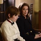 Zwei Personen sitzen auf einer Bank. Links: Ein Kind in Hemd und Fliege, rechts: Eine Frau in schwarzem Blazer, schaut das Kind an.