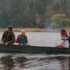 Vier Menschen in einem kleinen Boot auf einem See, umgeben von bewaldeter Landschaft. Ein Außenbordmotor ist sichtbar.