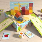 Wort "Haba", bunte Bausteine, Spielfahrzeug auf geöffneter Box, Bauillustration im Hintergrund, Karten mit Apfel und Brot.