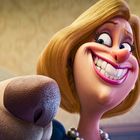 Ein Hund mit blauer Maske und eine Frau mit breitem Lächeln nebeneinander, in einem Raum mit gemusterter Tapete.