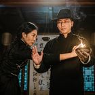 Chinesische Schriftzeichen auf Schriftrollen. Zwei Personen in traditioneller Kleidung; eine hält eine flammende Schale.