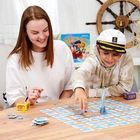 Ein Junge und eine Frau spielen ein Brettspiel; der Junge trägt eine Kapitänsmütze, im Hintergrund ein Steuerrad.