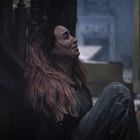 Eine Person mit langen Haaren sitzt verzweifelt auf dem Boden in einem dunklen, verfallenen Raum.