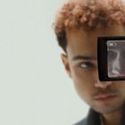 Auf dem Display der Kamera steht "REC". Ein Mann wird unscharf gesehen, sein Gesicht spiegelt sich im Kameradisplay.