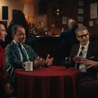 Text: Shawano Casino. Szene: Vier Männer sitzen um einen Tisch in einem gemütlichen, holzgetäfelten Raum mit Bar.