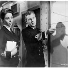 Eine Frau und ein Mann in Militäruniformen, der Mann zeigt mit einem Zeigestock auf eine Navigationskarte.