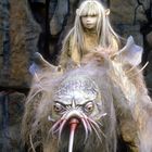 Eine Kreatur mit langen Haaren reitet auf einem haarigen, fremdartigen Wesen mit Tentakeln im Gesicht.