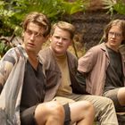 Drei junge Männer sitzen in einem dschungelartigen Umfeld und blicken überrascht seitlich. Sie tragen lässige Kleidung.