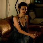 Keine Texte vorhanden. Eine Frau in einem eleganten Abendkleid sitzt auf einem Ledersofa mit einem Weinglas in der Hand.