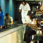 Eine Frau in blauer Uniform vor Filmteam auf Rollband. Kamera, Mikrofon, Crew in konzentrierter Aktion.