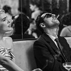 Eine Frau mit kurzen Haaren und gestreiftem Oberteil neben einem Mann, der raucht und eine Sonnenbrille trägt.