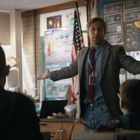 Ein Lehrer steht mit ausgebreiteten Armen vor Schülern in einem Klassenzimmer. Im Hintergrund Poster und die US-Flagge.
