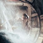 Zwei Personen in einem runden, metallischen Raum, von Wasser oder Dampf umgeben, wirken angespannt und erschrocken.