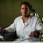 Person sitzt angespannt in einem metallenem Stuhl mit Armlehnen, trägt ein weißes Hemd.