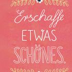 "Erschaffe etwas Schönes." steht in geschwungener Schrift. Verziert mit Blumenranken auf korallrotem Hintergrund.