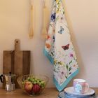 Tasse mit Aufschrift "Zeit für mich", Blumenmuster-Handtuch, Holzutensilien, Schneidebrett, Obstschale mit Äpfeln und Trauben.