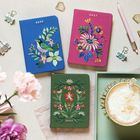Die Szene zeigt drei bunte Notizbücher mit "2027" bestickt. Eines ist blau mit Vogel, eines pink mit Blumen, eines grün mit Pflanzen.