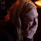 Eine Frau hält ihre Hand vor den Mund und scheint zu weinen, mit Tränen auf ihrer Wange.