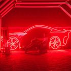 Leuchtende rote Umrisse eines Autos; ein Mann sitzt in einem Rennsimulator mit Lenkrad.