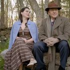 Ein Mann und eine Frau sitzen auf einer Bank im Wald, lächelnd und in eleganter Kleidung.