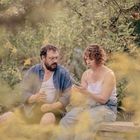 Keine sichtbaren Texte. Ein Mann und eine Frau sitzen in einem grünen Garten, umgeben von Pflanzen. Sie scheinen zu reden.