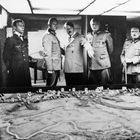 Sechs Männer in Militäruniform betrachten ein großflächiges militärisches Modell oder eine Karte.