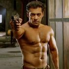 Oberkörperfreier Mann zielt mit Pistole in einem rustikalen Raum, im Hintergrund unscharf Werkzeuge und Kisten.