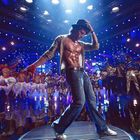 Ein Tänzer in glitzernder Kleidung mit Zylinder, umgeben von einer tanzenden Gruppe in bunter, schimmernder Kulisse.