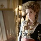 Eine Frau in historischer Kleidung steht vor einem Spiegel, im Hintergrund brennen Kerzen.