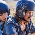 Zwei Personen auf einem Motorrad, beide mit Helmen; der vordere Helm hat Skelette als Illustrationen.