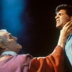 Zwei Männer in intensiver Szene; der ältere hält den jüngeren am Hals, beide wirken angespannt.