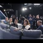 Eine Gruppe sitzt auf einem grauen Sofa in einem TV-Studio, umgeben von Kameras und Crew.