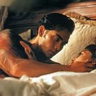 Es gibt keine sichtbaren Texte. Ein tätowierter Mann liegt im Bett und berührt zärtlich das Gesicht einer Frau.